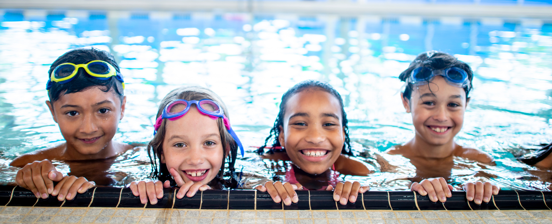 smiling kids peeking out the side of an indoor swimming pool